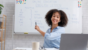 Professeur face à un ordinateur qui pointe un tableau avec écrit un cours d'anglais dessus