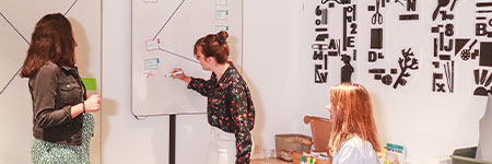Trois membres de l'équipe marketing d'acadomia font une réunion brainstorming en écrivant sur un tableau