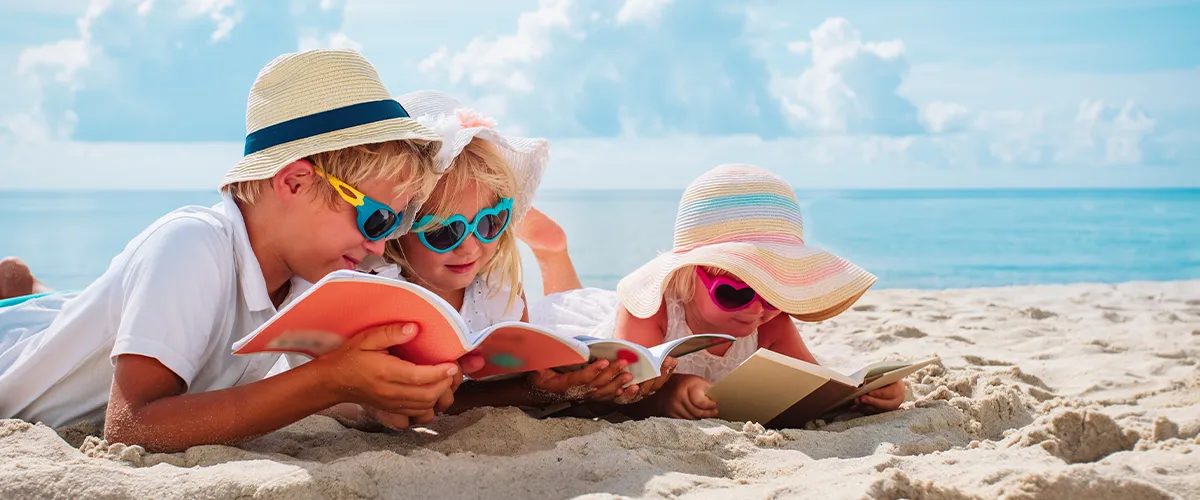Trois enfants de primaire sur leurs cahiers de vacances pendant les vacances d'été - Acadomia