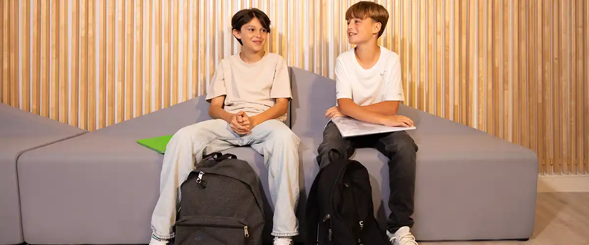 Deux collégiens souriants discutent ensemble sur un canapé dans un espace d'accueil Acadomia - photo tous droits réservés