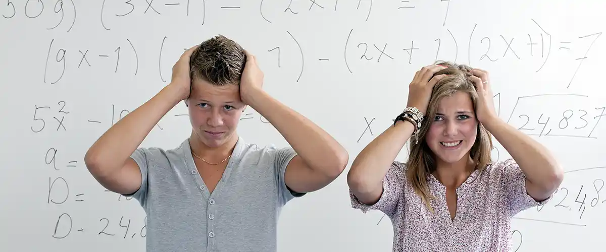 Deux lycéens stressés se tenant la tête devant un tableau de mathématiques dans une salle de cours Acadomia