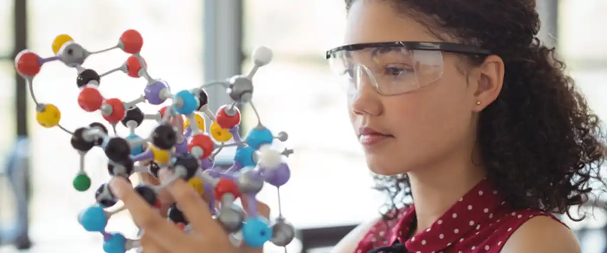 Une lycéenne concentrée examine un modèle moléculaire lors d'un cours de chimie dans une salle Acadomia