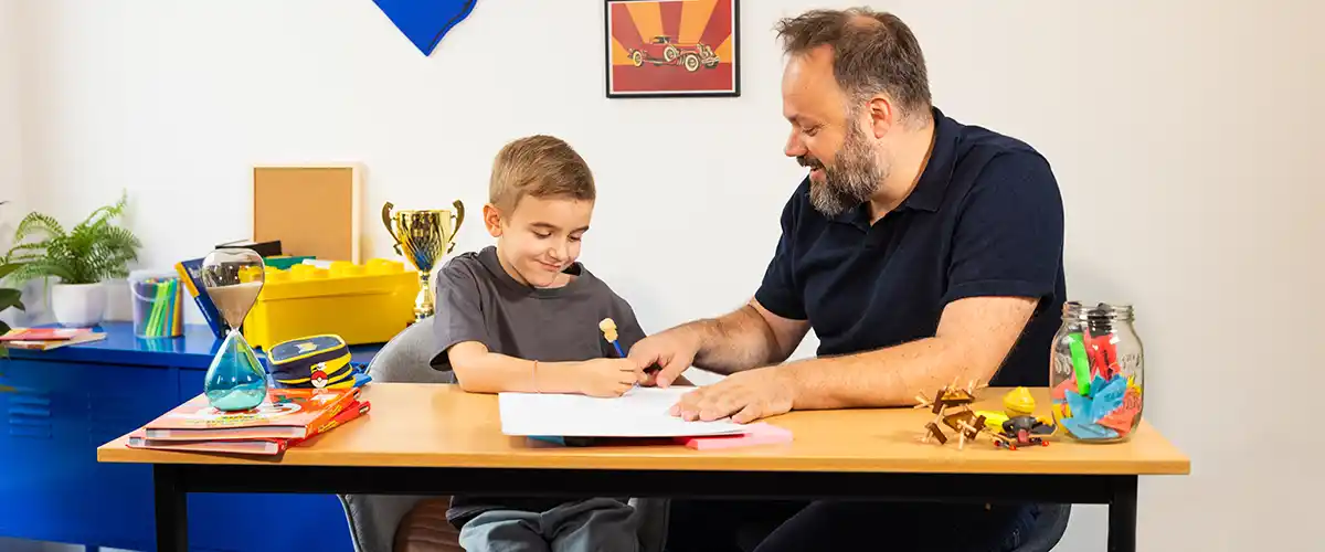 Un père et son fils concentrés travaillent ensemble sur un exercice d'écriture dans une chambre d'enfant - photo tous droits réservés