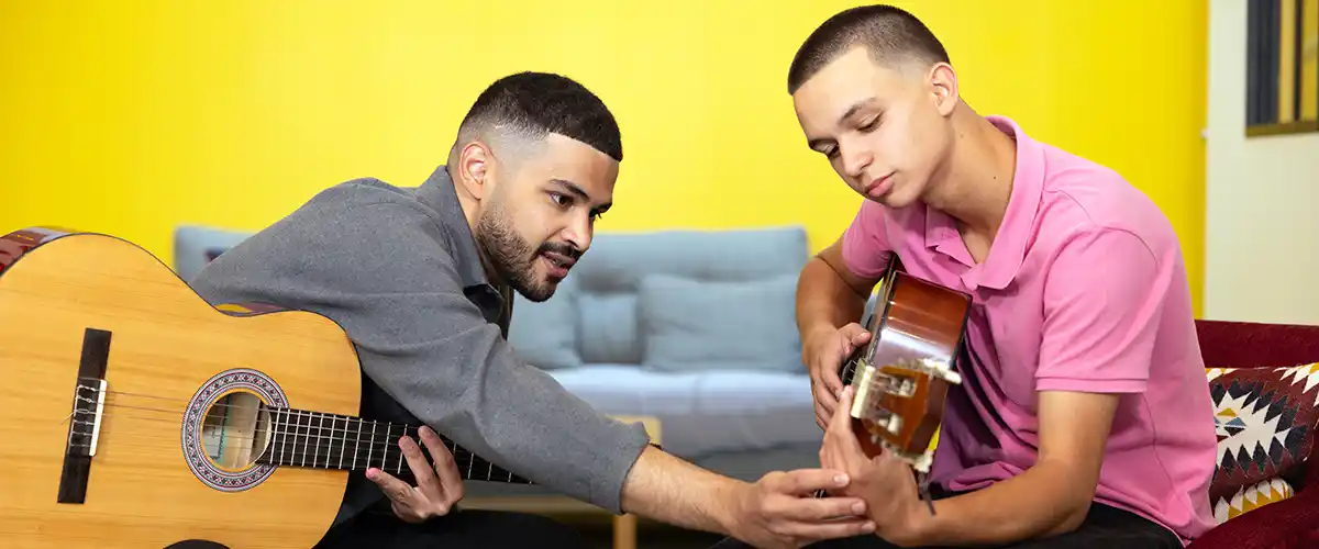Un professeur Acadomia guide un lycéen concentré dans l'apprentissage de la guitare lors d'un cours particulier à domicile - photo tous droits réservés