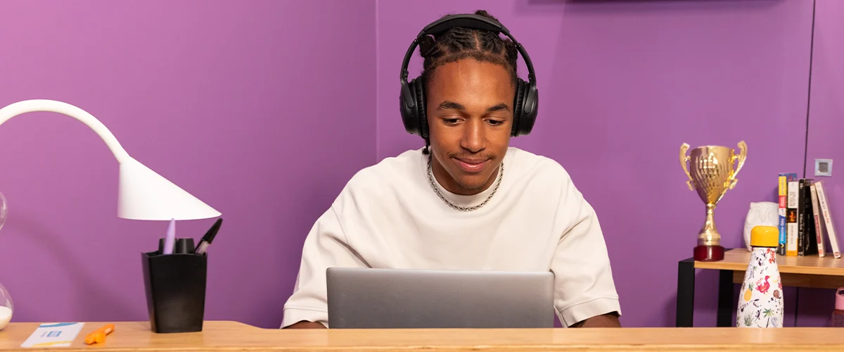 Un lycéen concentré travaille sur son ordinateur portable avec un casque audio dans un environnement de travail personnel - photo tous droits réservés