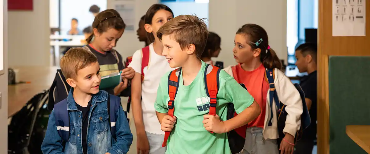 Groupe d'élèves de primaire souriants se déplaçant dans un couloir d'école avec leurs cartables - photo tous droits réservés