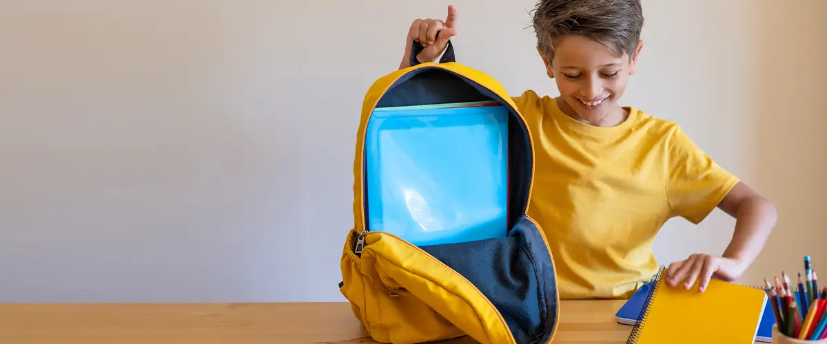 Un collégien souriant prépare son sac à dos avec ses fournitures scolaires dans un environnement studieux Acadomia