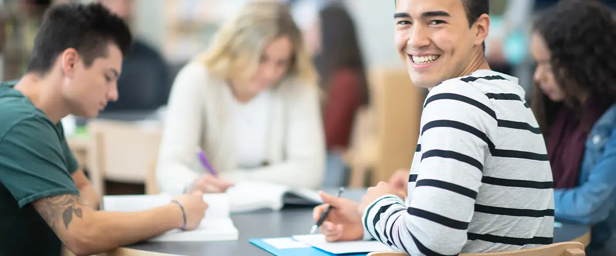 Groupe d'étudiants studieux travaillant ensemble dans une salle de cours Acadomia, un jeune homme souriant au premier plan