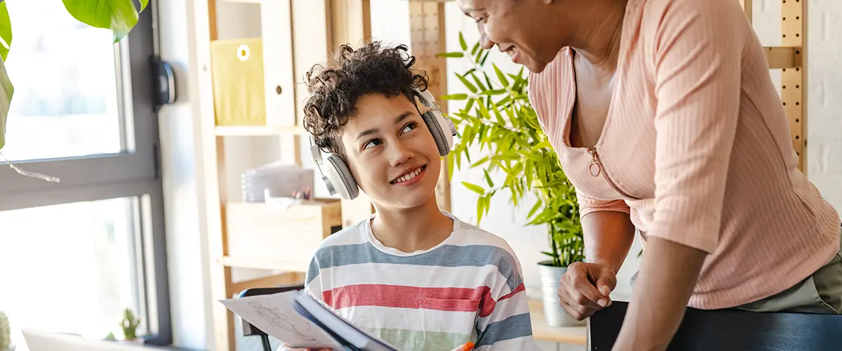 Un collégien souriant portant un casque audio échange avec une enseignante Acadomia lors d'une séance de soutien scolaire à domicile