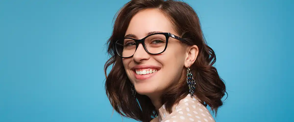 Jeune femme souriante portant des lunettes posant avec assurance sur fond bleu