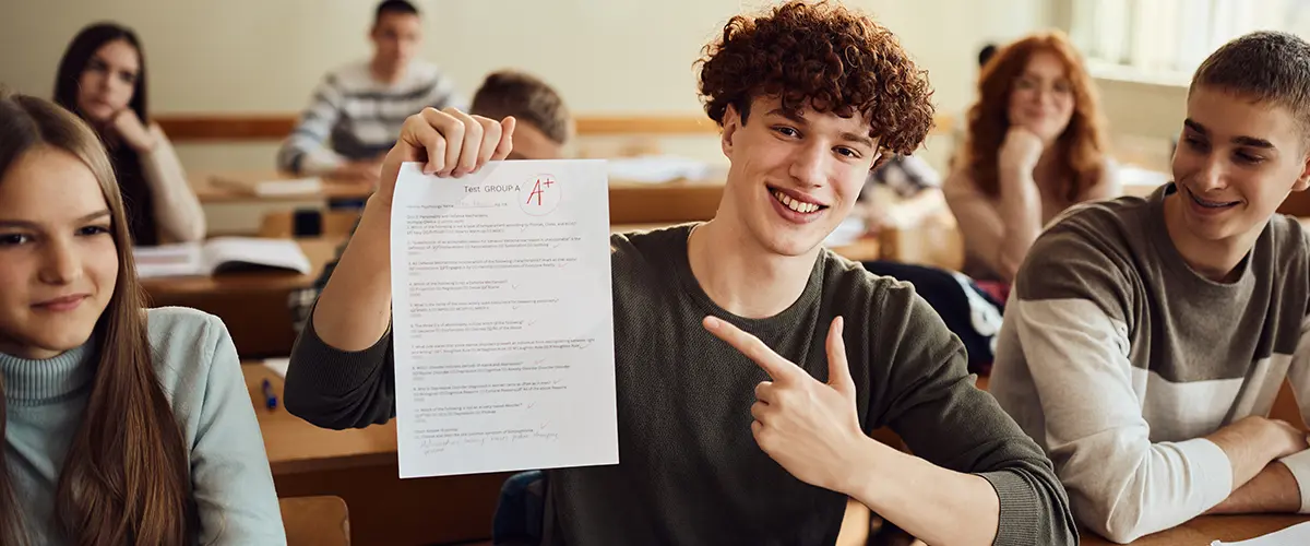 Un lycéen souriant et fier présente son test noté A+ à ses camarades dans une salle de classe Acadomia