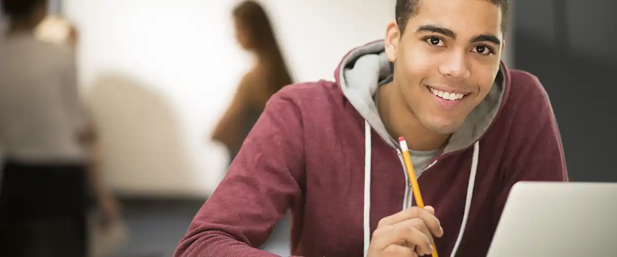 Un lycéen souriant tient un crayon devant son ordinateur portable dans une salle de cours Acadomia