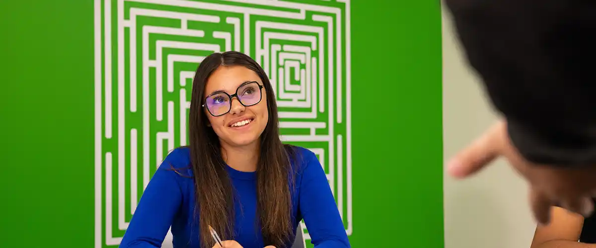 Une jeune femme souriante portant des lunettes échange avec un interlocuteur dans un espace Acadomia au décor moderne - photo tous droits réservés