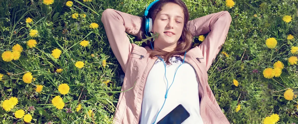 Une adolescente détendue écoute de la musique allongée dans un champ de pissenlits lors d'une pause révisions