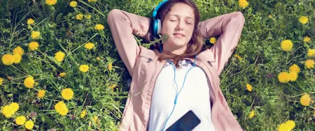 Une adolescente détendue écoute de la musique allongée dans un champ de pissenlits lors d'une pause révisions