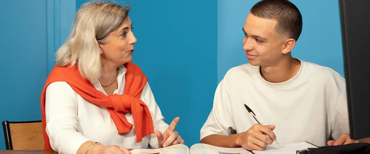 Une enseignante Acadomia explique une notion à un lycéen attentif prenant des notes dans une salle de cours - photo tous droits réservés