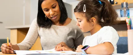 Une enseignante Acadomia accompagne une élève de primaire concentrée dans ses exercices lors d'un cours particulier à domicile - photo tous droits réservés