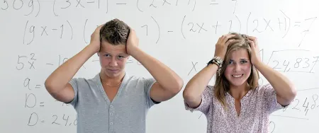 Deux lycéens stressés se tenant la tête devant un tableau de mathématiques dans une salle de cours Acadomia