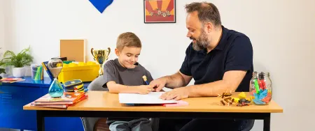 Un père et son fils concentrés travaillent ensemble sur un exercice d'écriture dans une chambre d'enfant - photo tous droits réservés