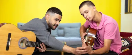 Un professeur Acadomia guide un lycéen concentré dans l'apprentissage de la guitare lors d'un cours particulier à domicile - photo tous droits réservés