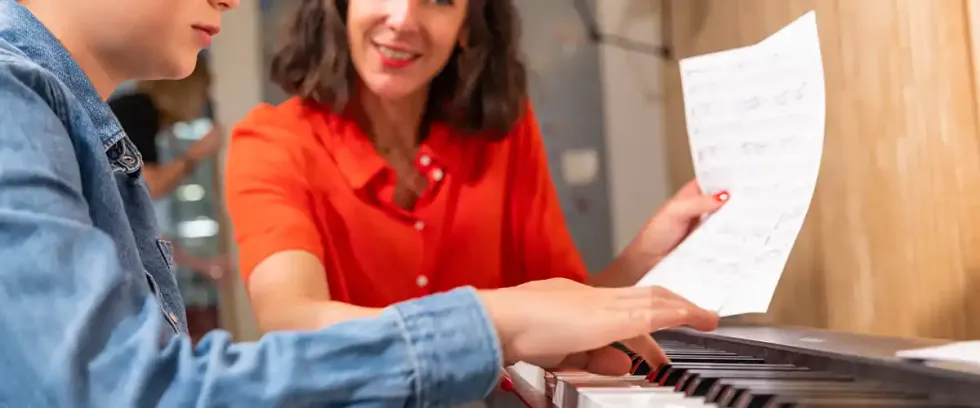 Une enseignante Acadomia souriante accompagne un élève au piano lors d'un cours de musique à domicile - photo tous droits réservés