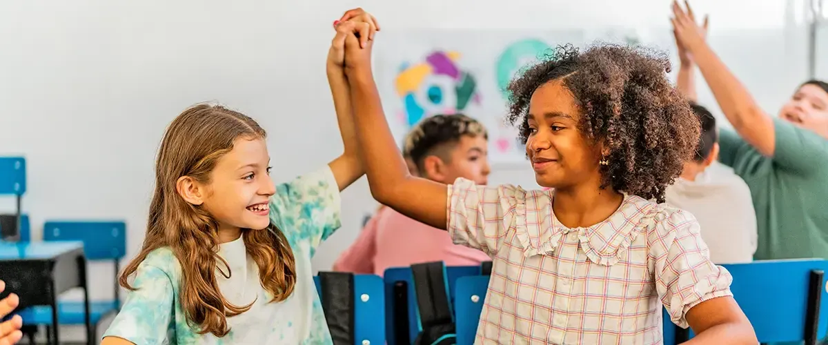 Deux collégiennes souriantes lèvent leurs mains jointes en signe de victoire dans une salle de classe Acadomia