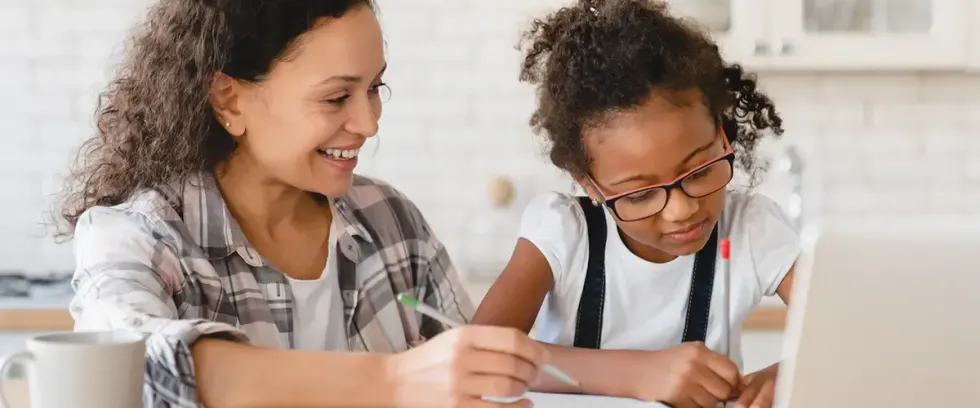 Une mère souriante accompagne sa fille concentrée dans ses devoirs à la maison