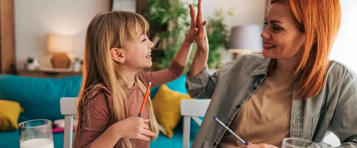 Une élève de primaire souriante tape dans la main de son enseignante Acadomia après un exercice réussi lors d'un cours particulier à domicile