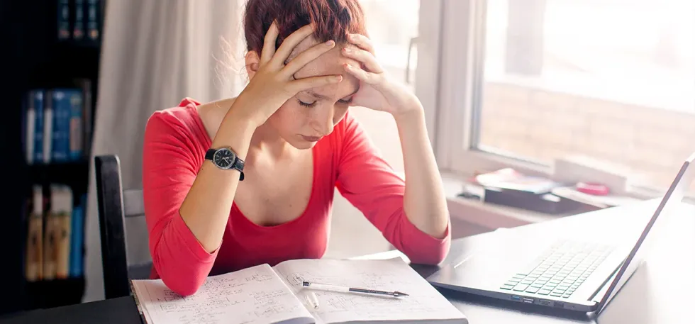 Une lycéenne stressée se tient la tête face à ses révisions dans un espace de travail à domicile