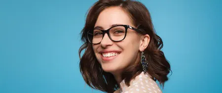 Jeune femme souriante portant des lunettes posant avec assurance sur fond bleu