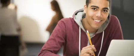 Un lycéen souriant tient un crayon devant son ordinateur portable dans une salle de cours Acadomia