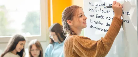Une collégienne souriante écrit une phrase en français au tableau dans une salle de cours Acadomia